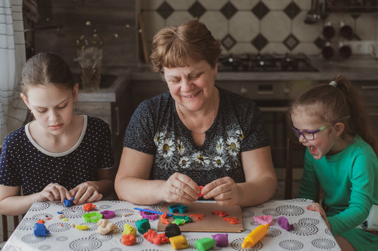 An adult woman and two little girls make plasticine figurines at home. Grandmother and granddaughters are sitting at home. Family Values Concept