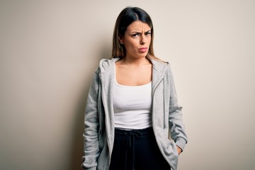 Young beautiful brunette sportswoman wearing sportswoman training over white background skeptic and nervous, frowning upset because of problem. Negative person.