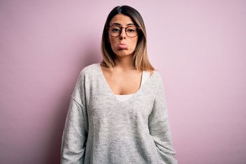 Fototapeta premium Young beautiful brunette woman wearing casual sweater and glasses over pink background depressed and worry for distress, crying angry and afraid. Sad expression.