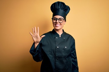 Young beautiful brunette chef woman wearing cooker uniform and hat over yellow background showing...