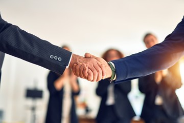 Group of business workers smiling happy and confident. Two of them, standing with smile on face shaking hands for agreement. Partners applauding at the office.