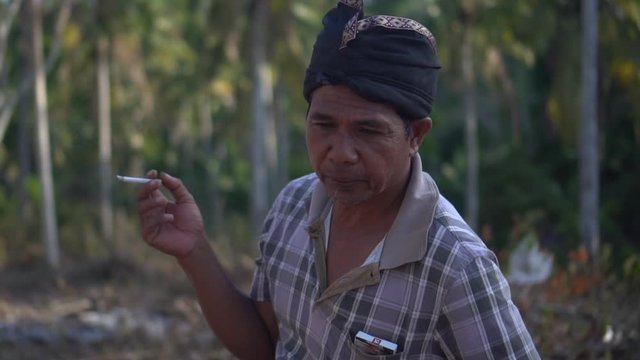 Close up shot of a traditional balinese male spiting and smoking in slow motion.