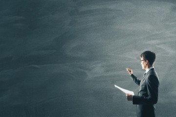 Businessman with document in hand drawing on blank blackboard.