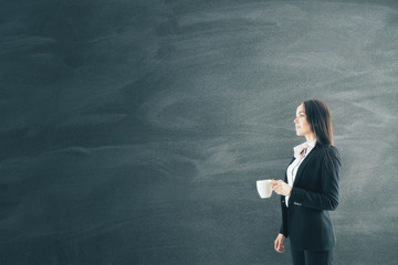 Businesswoman with cup of coffee in hand and blank blackboard.