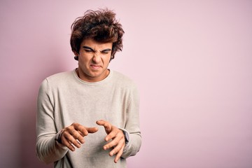 Young handsome man wearing casual t-shirt standing over isolated pink background disgusted...