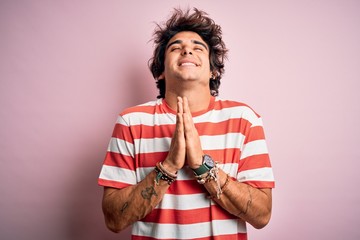 Young handsome man wearing striped casual t-shirt standing over isolated pink background begging...
