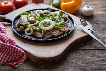 Fried meat on iron plate with rustic wooden background