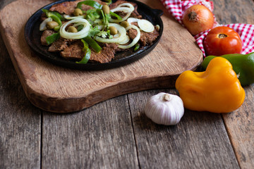 Fried meat on iron plate with rustic wooden background