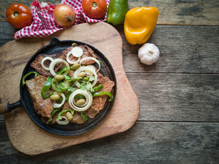 Fried meat on the iron plate with rustic wooden background. Flat lay.