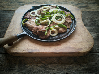 Fried meat on the iron plate. Rustic wood background.