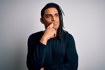 Young handsome african american man with dreadlocks wearing black casual sweater with hand on chin thinking about question, pensive expression. Smiling with thoughtful face. Doubt concept.