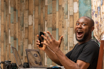young black man working with his laptop and mobile phone feeling happy and excited celebrating