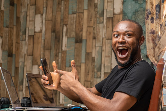 young black man working with his laptop and mobile phone feeling happy and excited pointing to his phone