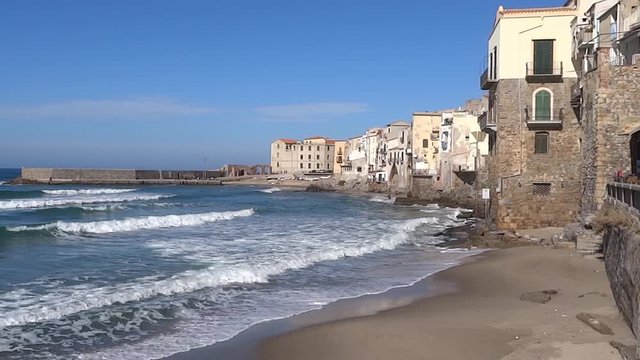 Beautiful empty beach, blue sea with white waves, old historical houses in the recreational city Cefalu on Sicily island, Italy 