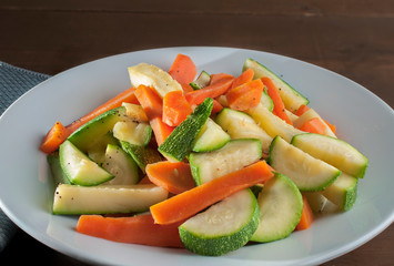 zucchini and carrots on a white plate with salt pepper and a touch of butter.