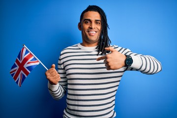 Young african american patriotic man with dreadlocks holding united kingdom flag with surprise face pointing finger to himself