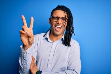 Naklejka premium Young handsome african american man with dreadlocks wearing casual shirt and glasses smiling with happy face winking at the camera doing victory sign. Number two.