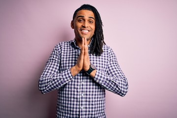 Young handsome african american afro man with dreadlocks wearing casual shirt praying with hands together asking for forgiveness smiling confident.