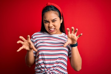 Young beautiful asian girl wearing casual striped t-shirt over isolated red background smiling funny doing claw gesture as cat, aggressive and sexy expression