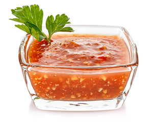 Hot tomato sauce with parsley leaves in a small transparent glass square bowl isolated on white background
