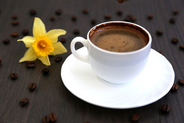 Morning coffee, spilled coffee beans, two cups of coffee, wooden table, flowers, daffodils.