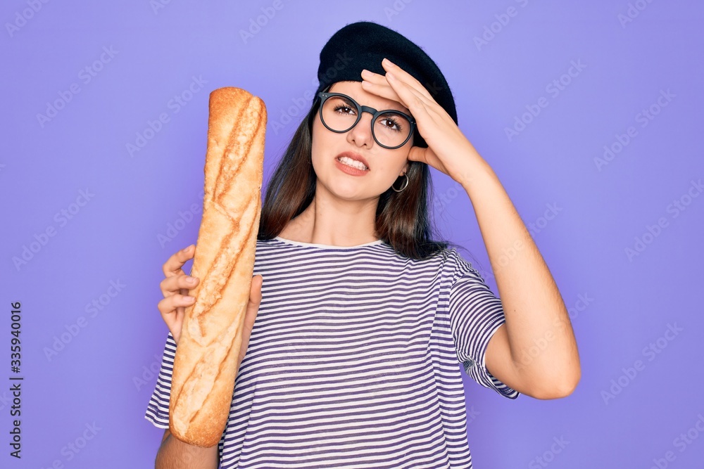 Poster Young beautiful girl wearing fashion french beret holding fresh baked bread baguette stressed with hand on head, shocked with shame and surprise face, angry and frustrated. Fear and upset for mistake.