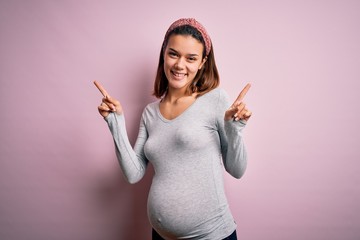Young beautiful teenager girl pregnant expecting baby over isolated pink background smiling confident pointing with fingers to different directions. Copy space for advertisement