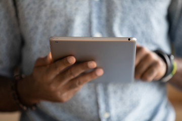 Close up of African American man browsing surfing wireless Internet on modern tablet gadget,...
