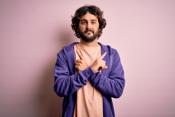 Young handsome sporty man with beard wearing casual sweatshirt over pink background Pointing to both sides with fingers, different direction disagree