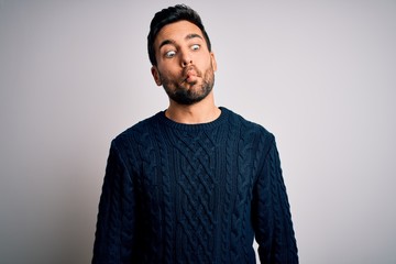 Obraz premium Young handsome man with beard wearing casual sweater standing over white background making fish face with lips, crazy and comical gesture. Funny expression.