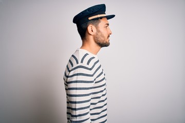 Young handsome sailor man with beard wearing navy striped uniform and captain hat looking to side,...