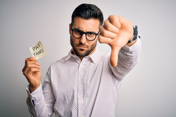 Young handsome man holding reminder paper with pay taxes message over white background with angry...