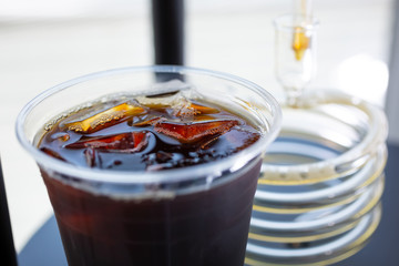 A closeup view of a clear plastic cup of coffee next to a spiral glass tube that is part of a Kyoto drip machine.