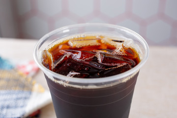A closeup view of a clear plastic cup full of ice cold coffee, in a restaurant or kitchen setting.