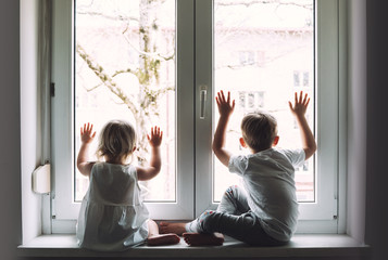 Little children are at home in quarantine and look out the window.