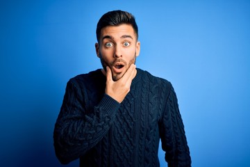 Young handsome man wearing casual sweater standing over isolated blue background Looking fascinated...