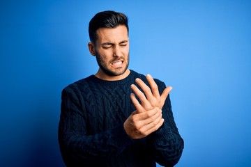 Young handsome man wearing casual sweater standing over isolated blue background Suffering pain on...