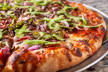 A closeup view of a supreme pizza pie, in a restaurant or kitchen setting.