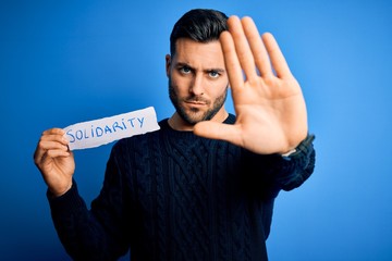 Young handsome man holding paper with solidarity message over blue background with open hand doing...