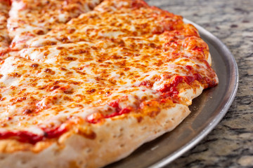 A closeup view of a plain cheese pizza pie on a steel pan, in a restaurant or kitchen setting.
