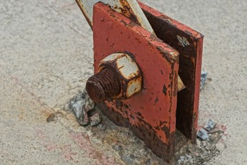 one brown rusty bolt with nut on a red iron plate in the street