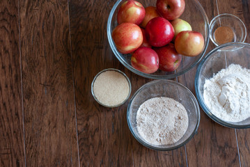 Apple pie ingredients in separate bowls positioned on a dark wood background