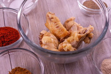 Glass bowl of chicken wings surrounded by glass bowls of spices