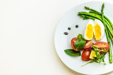 Boiled poached egg, cherry tomatoes, mix salad and asparagus on a white plate on an isolated white background. Healthy Diet Food Concept