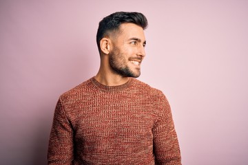 Fototapeta premium Young handsome man wearing casual sweater standing over isolated pink background looking away to side with smile on face, natural expression. Laughing confident.