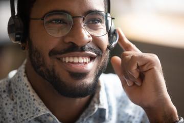 Close up of smiling African American male call center agent in glasses and wireless headset consult...