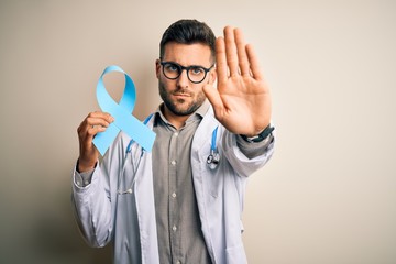 Young professional doctor man holding colon awareness blue ribbon over isolated background with...