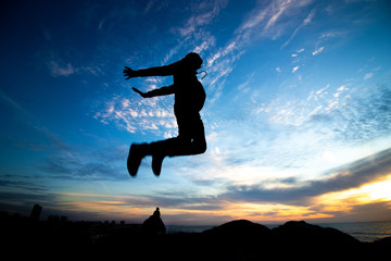 Fototapeta premium Silhouette of the boy jumping up against sunset at the beach,