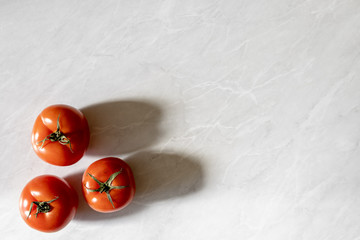 Fresh whole ripe tomatos on grey marble background wit long shadow and with copy space. Summer organic vegetable for salad.