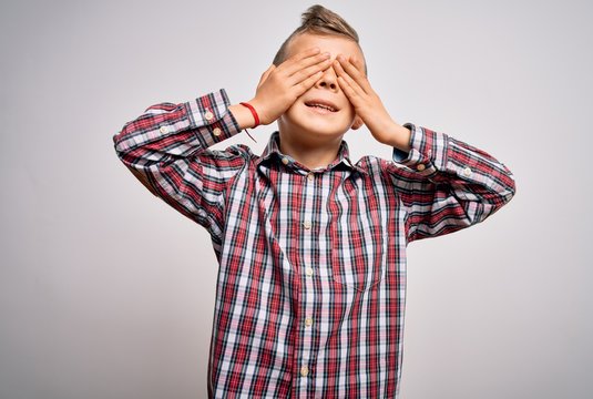 Young little caucasian kid with blue eyes wearing elegant shirt standing over isolated background covering eyes with hands smiling cheerful and funny. Blind concept.